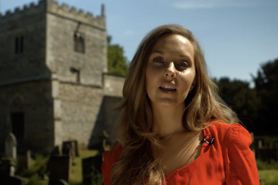 portrait photo of Dr Emma standing in front of a church in a red top