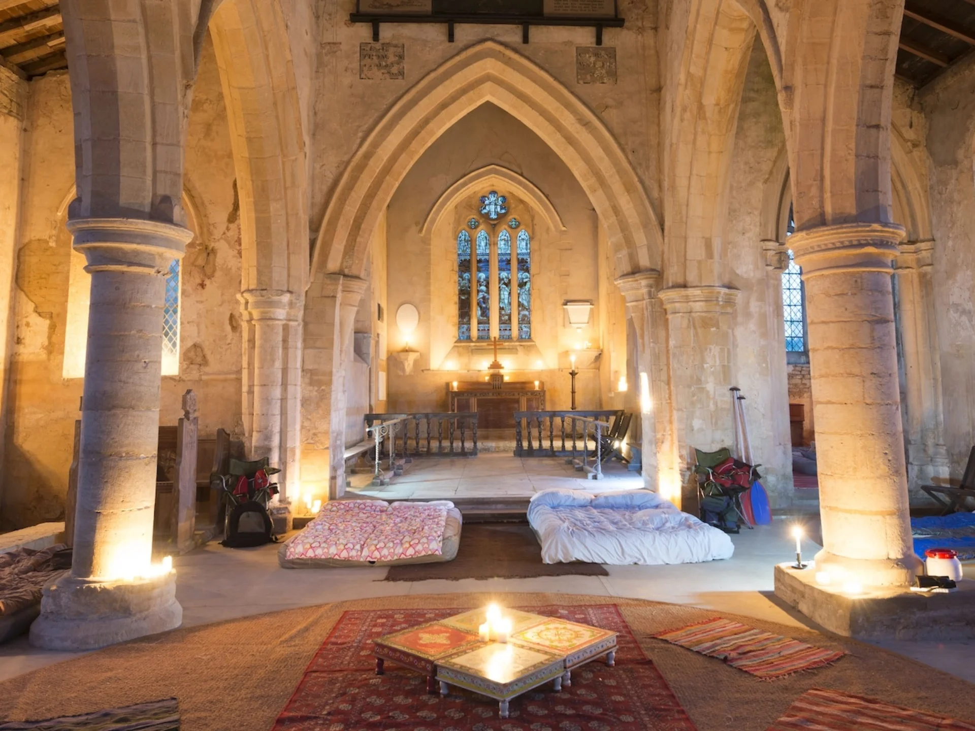 candle lit church interior with beautiful stone arches and large windows. Mattresses on floor.