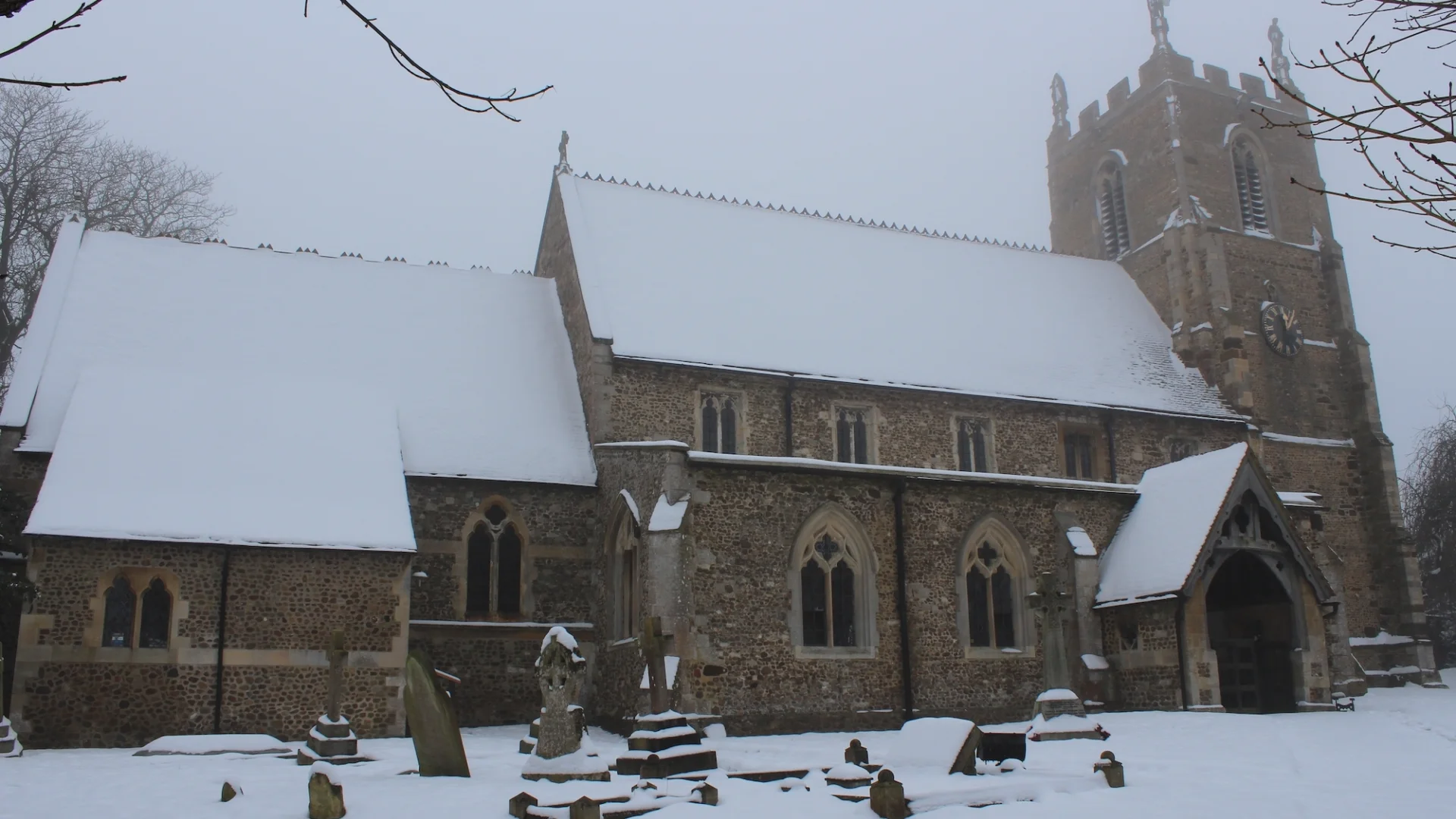 View from outside of the front of the church in the snow also showing some gravestones.
