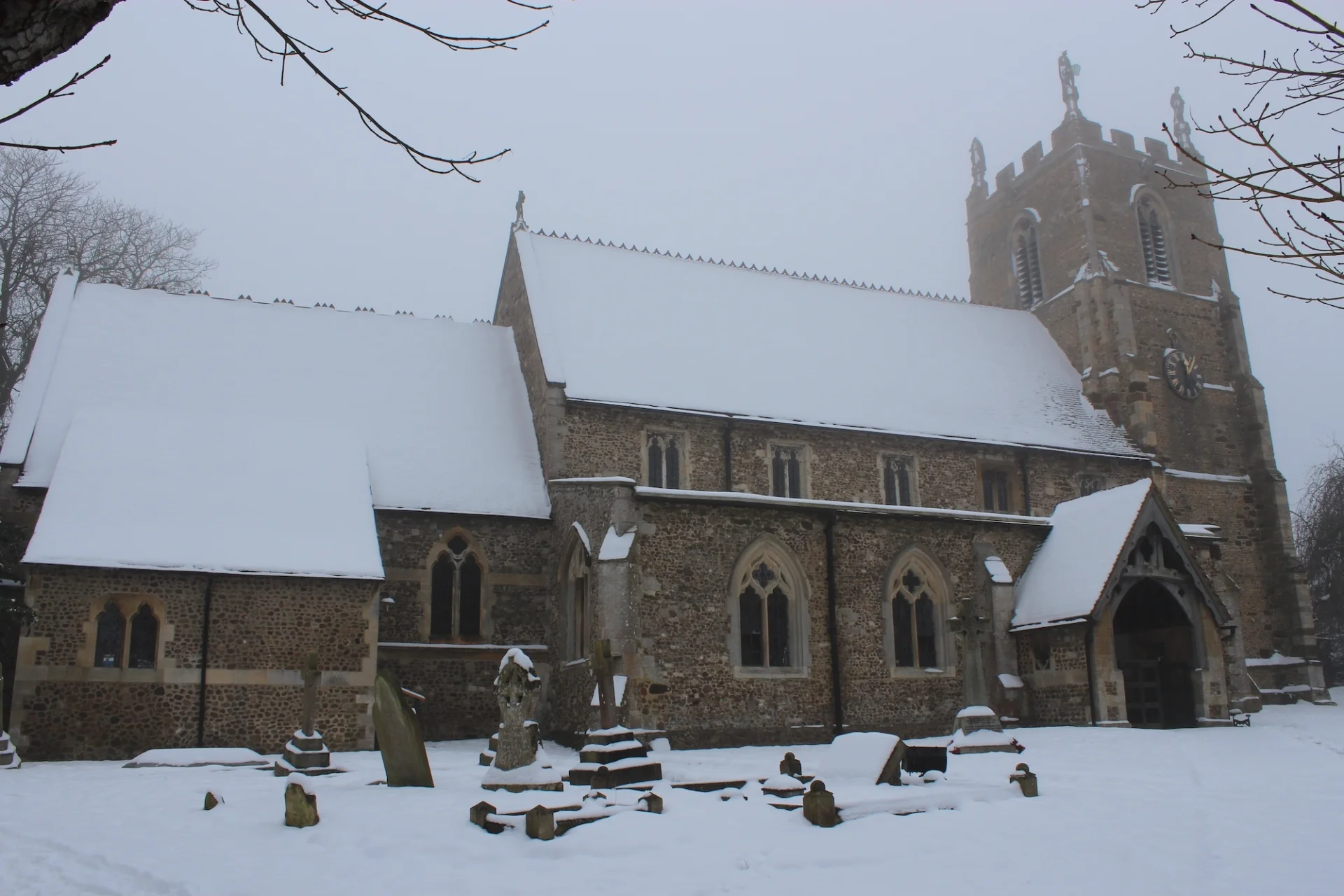 View from outside of the front of the church in the snow also showing some gravestones.