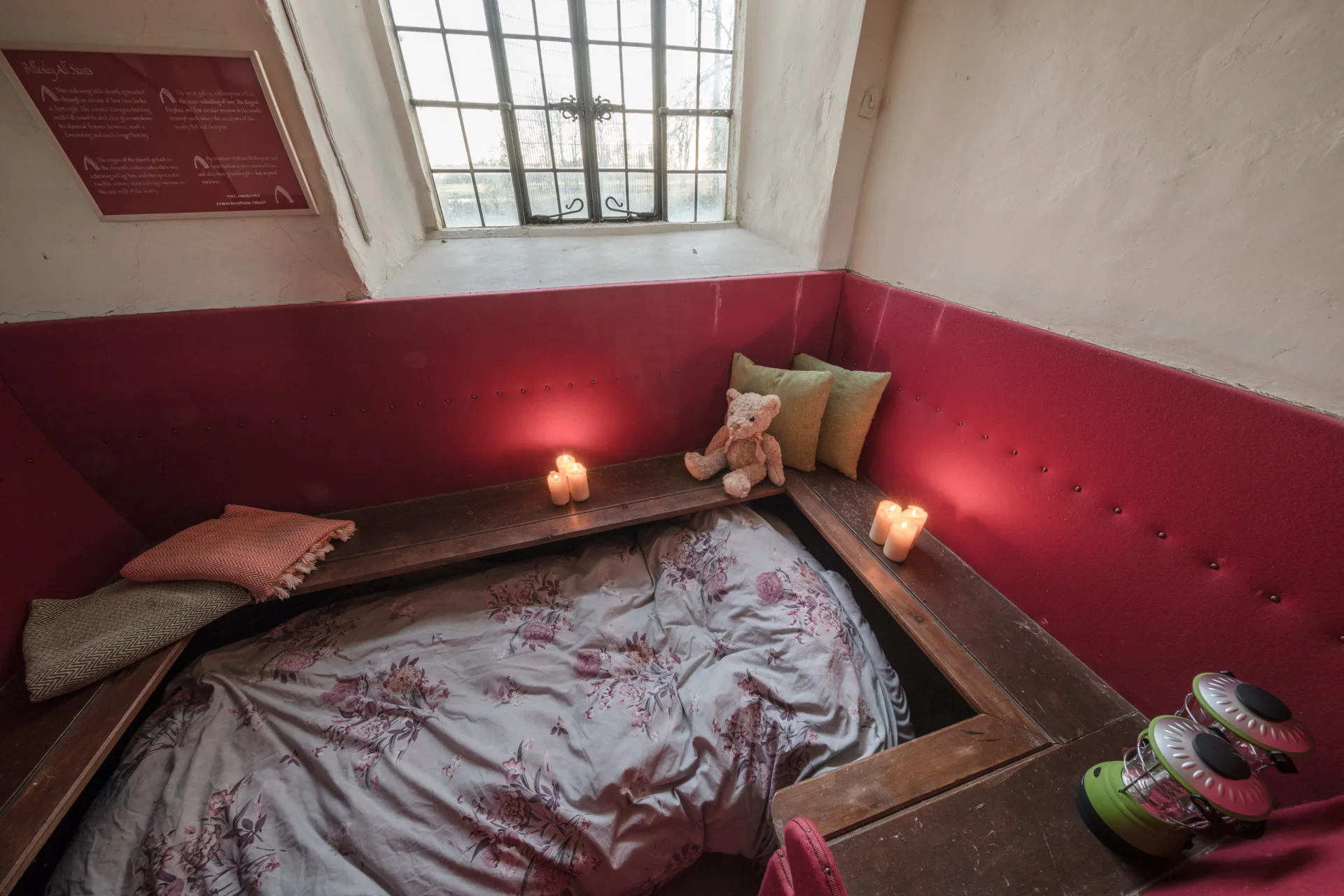 Church set up for champing with cosy bed with candles and teddy bears.