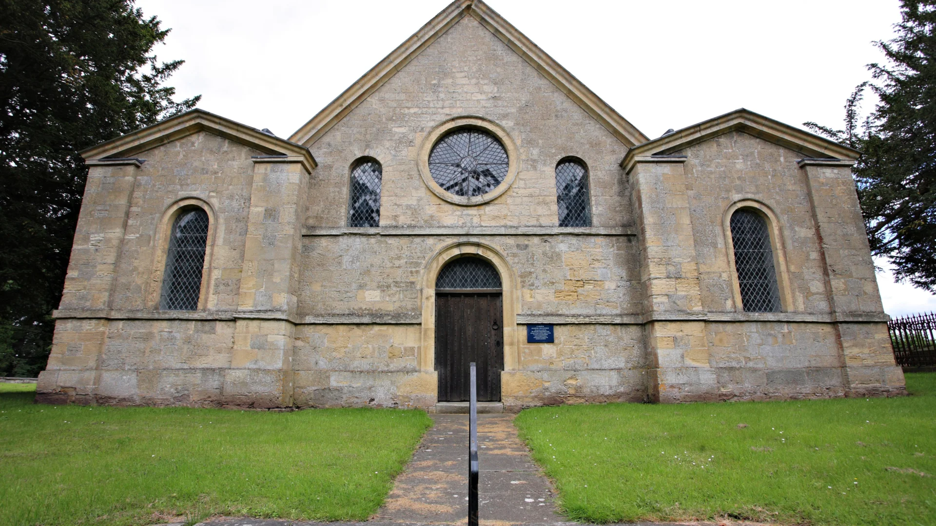 Symmetrical neo-Norman style west front with round central window