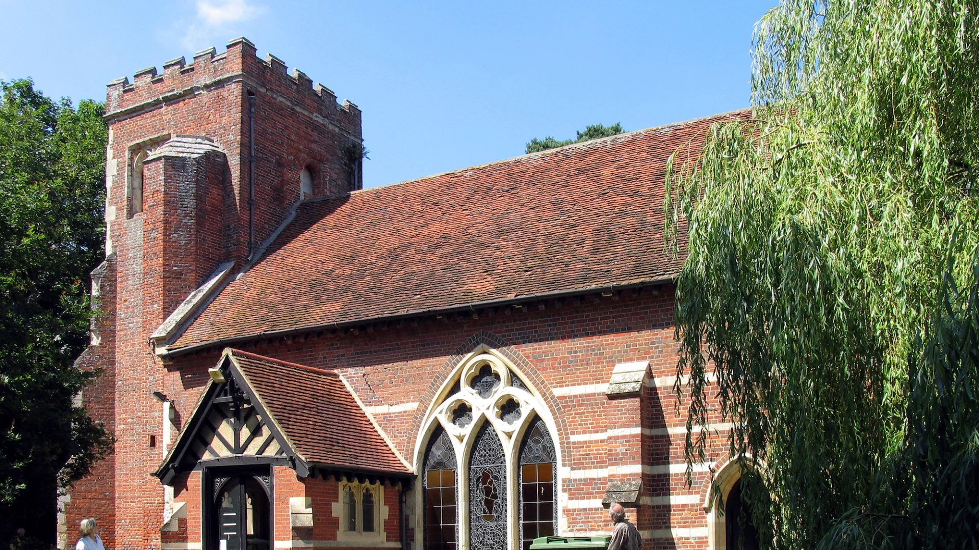 Tudor brick church exterior with large stained glass window next to the entrance way.