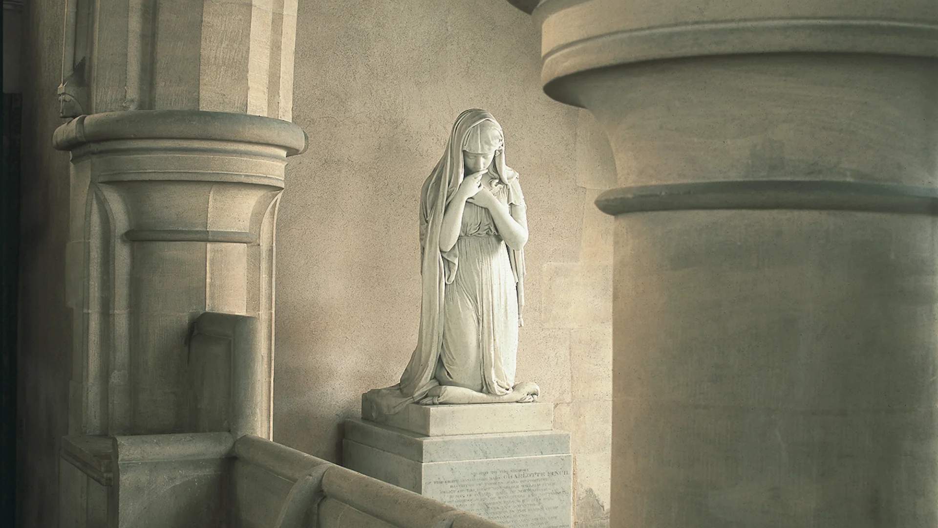 Beautiful marble statue of a woman with her hands to her lips and chest with veil pulled back. The statue is at the side of the church between the arches.