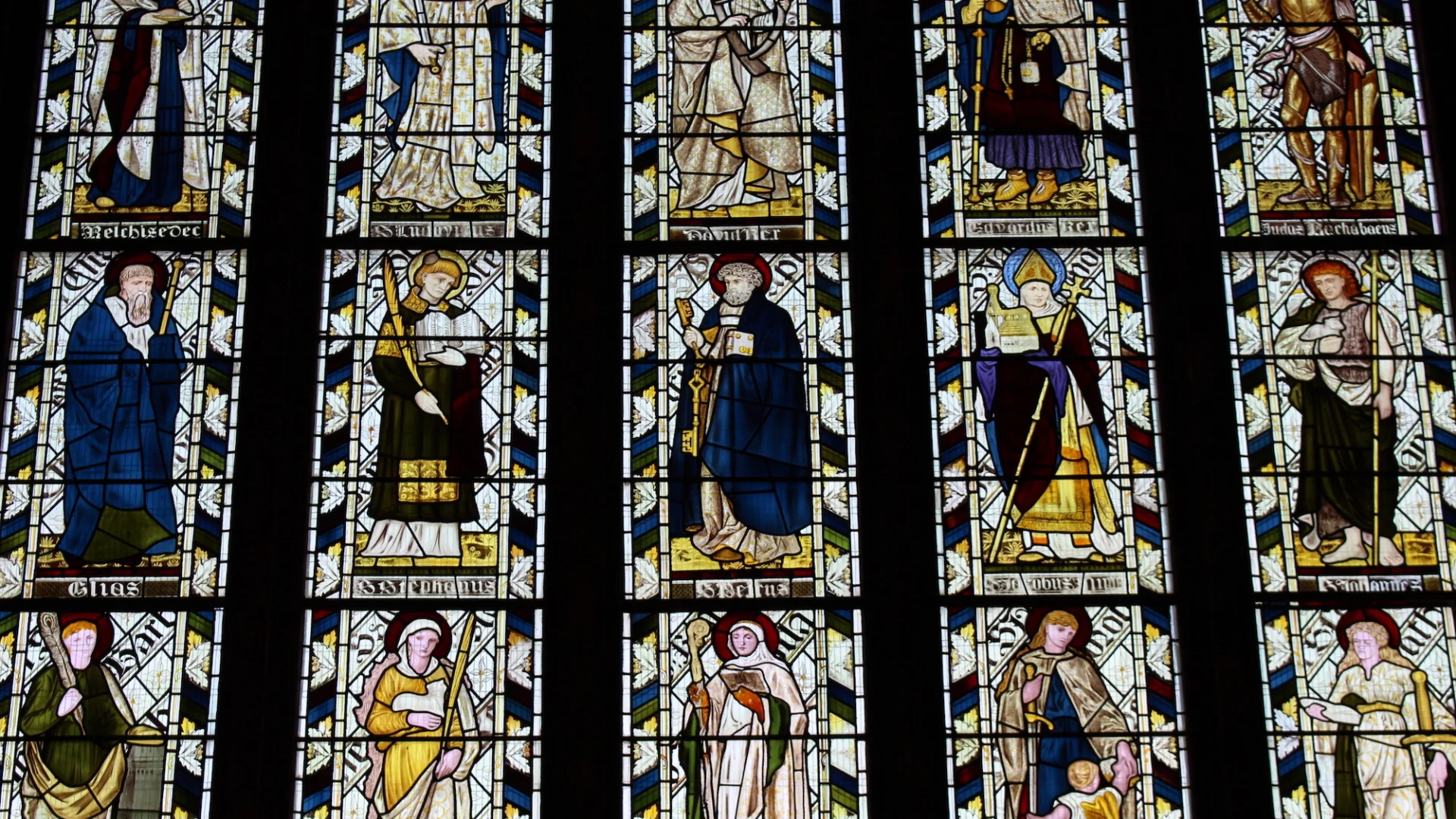 Highly decorated stained glass window in five parts depicting rows of figures - names not discernible in image.