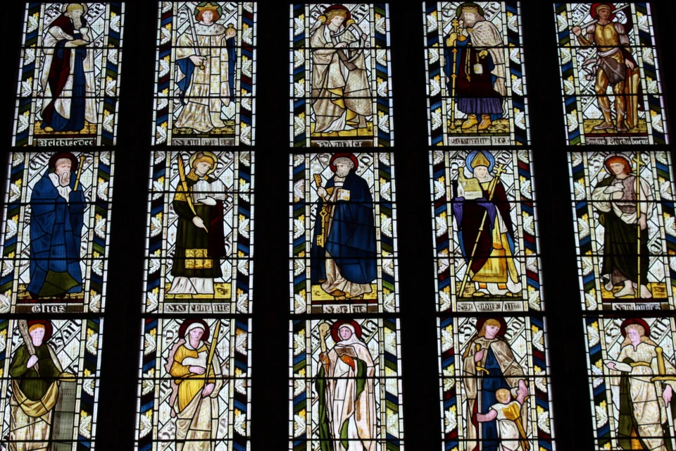Highly decorated stained glass window in five parts depicting rows of figures - names not discernible in image.