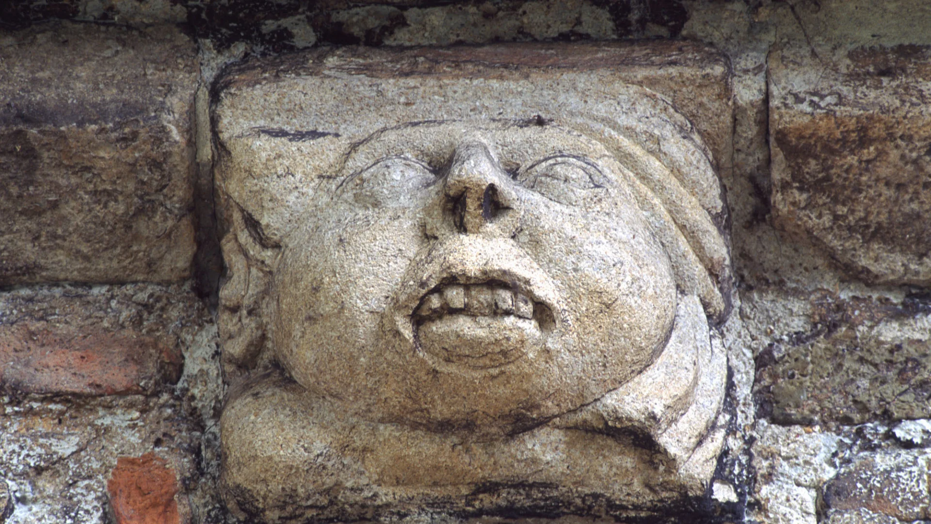 Corbel possibly C14th re-set above east window arch during the C18th restoration shows a human face with large exposed teeth