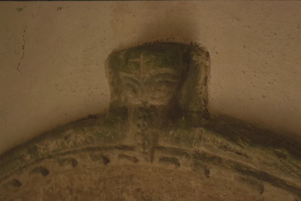 Stone carving on top of archway showing a face with cross etched on the head and a beard
