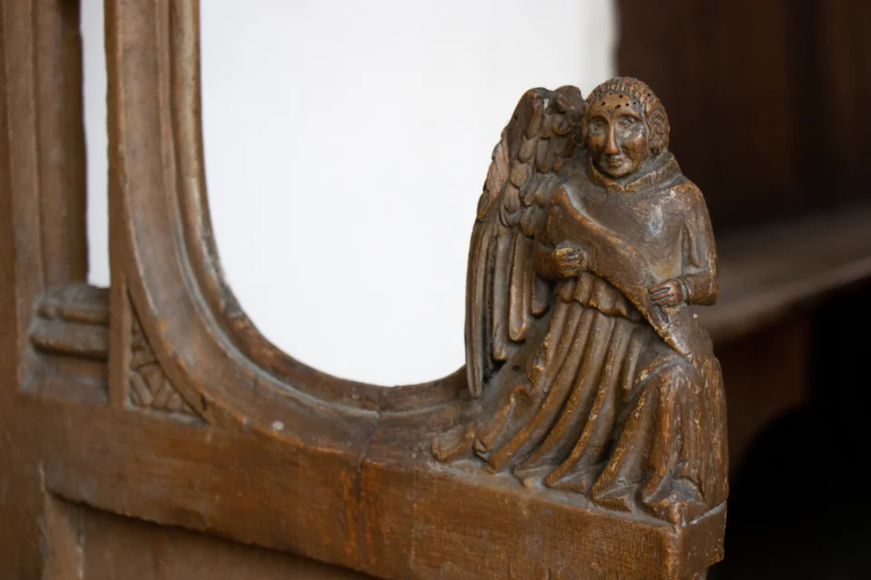 Angel poppyhead on pew in robes holding a script
