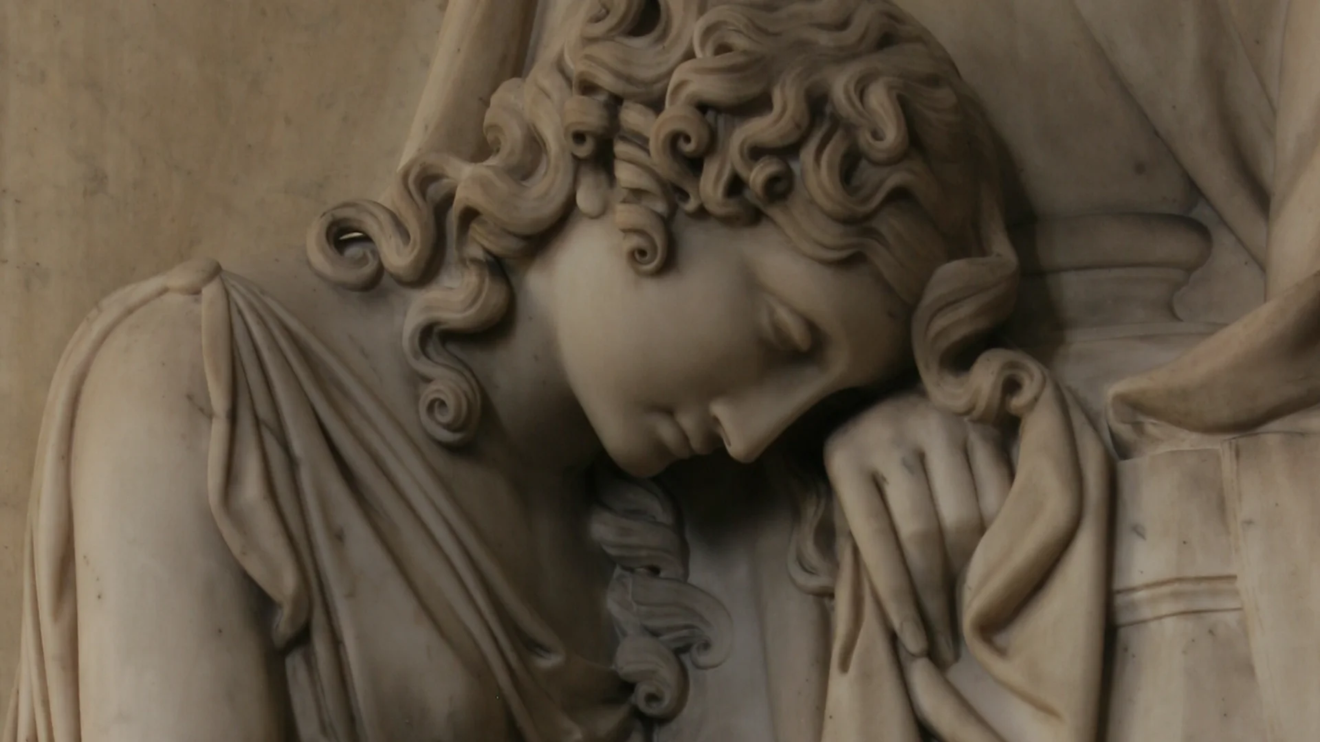 Statue of woman's face leaning with head on hand wearing greek robes