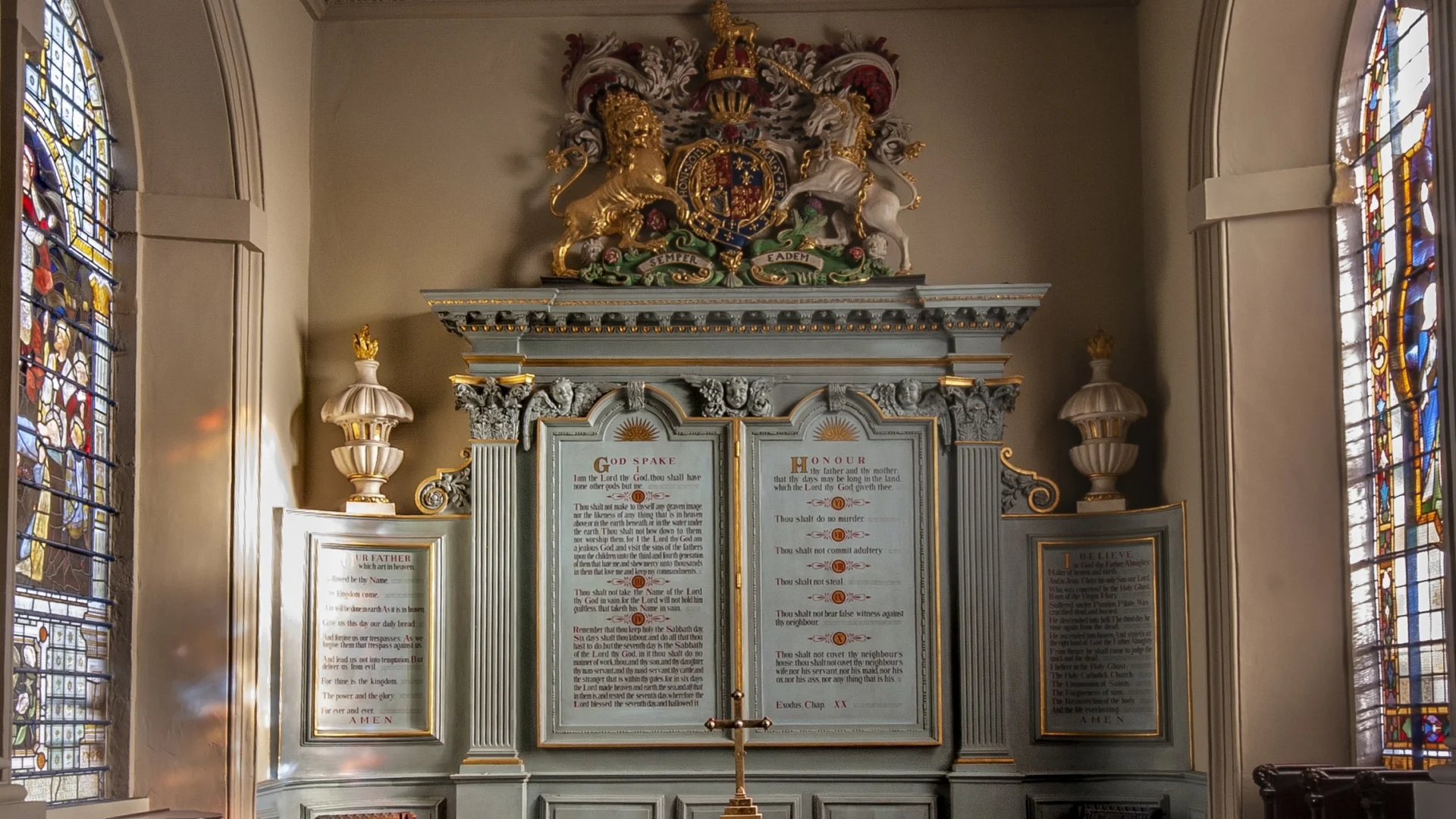 Interior 17th-century chancel with enormous blue memorial behind the altar, topped with a large royal coat of arms and colourful stained glass on either side.