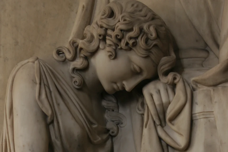Statue of woman's face leaning with head on hand wearing greek robes