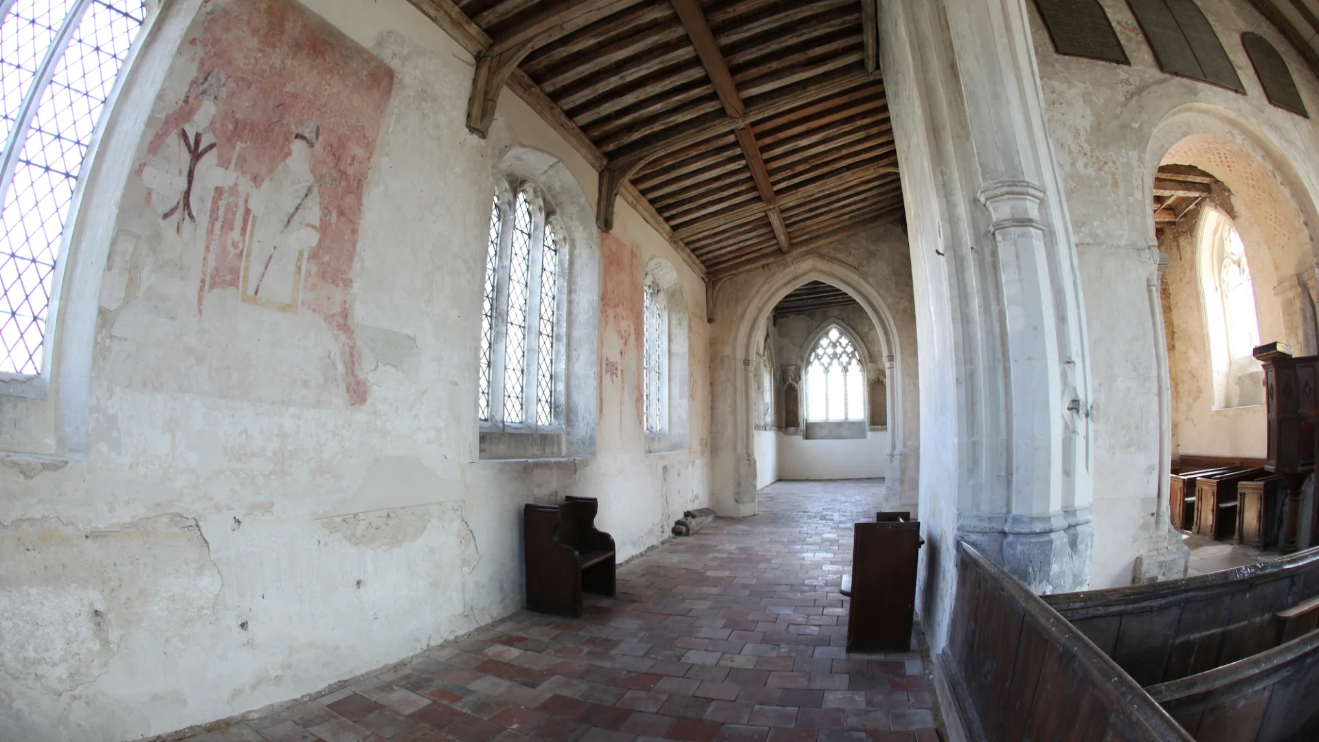 Interior showing wall paintings in red of two figures. Simple archways and decorative stone carved window