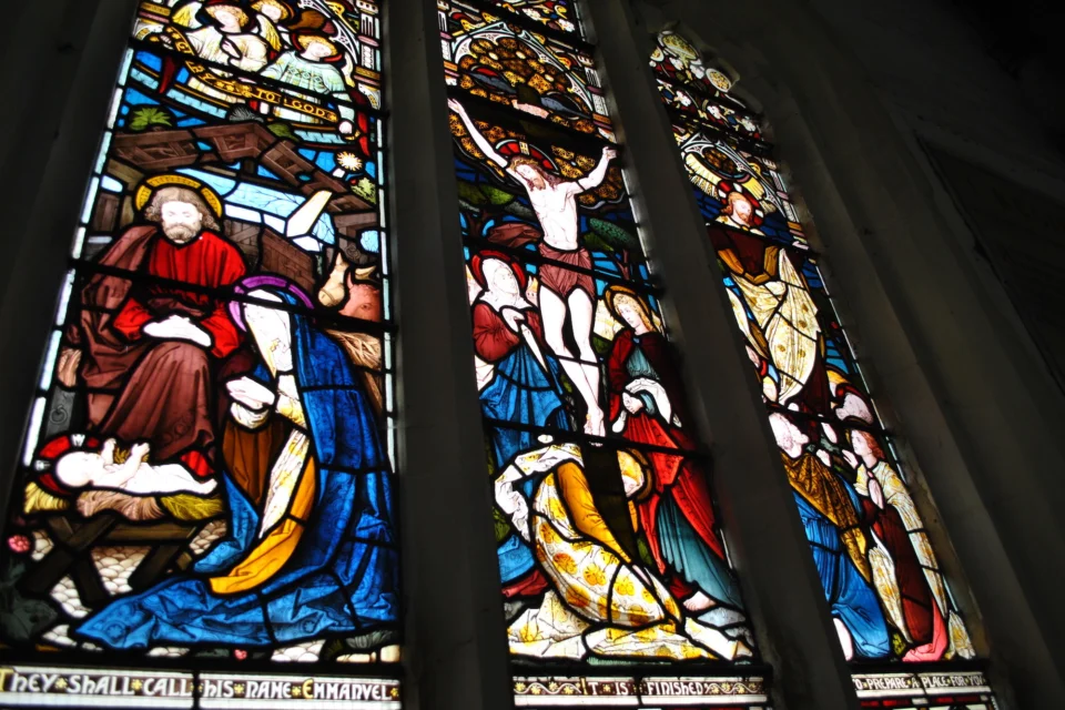 Colourful stained glass in rich blues, reds and yellows showing the birth, crucifixion and ascension of Christ
