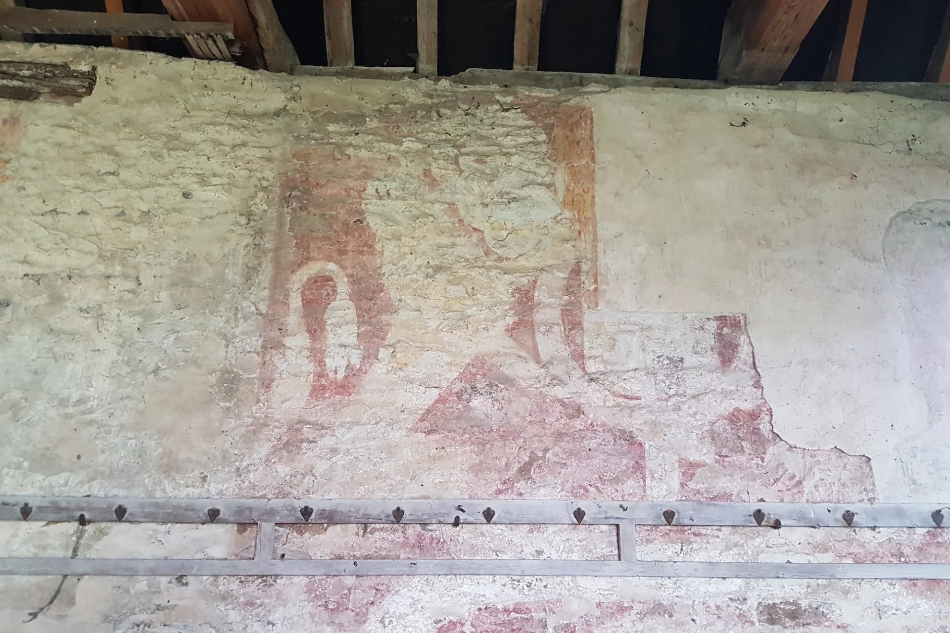 a large wallpainting of a faded lion with red outline on the interior wall of the nave