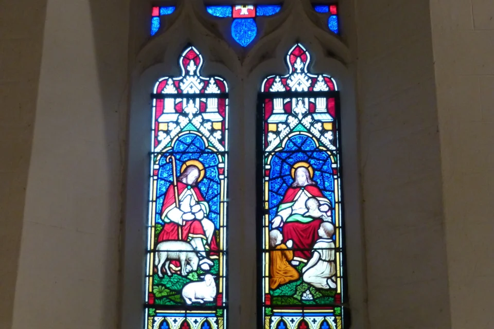 Two stained glass windows in bright colours depicting Christ with lambs and young children