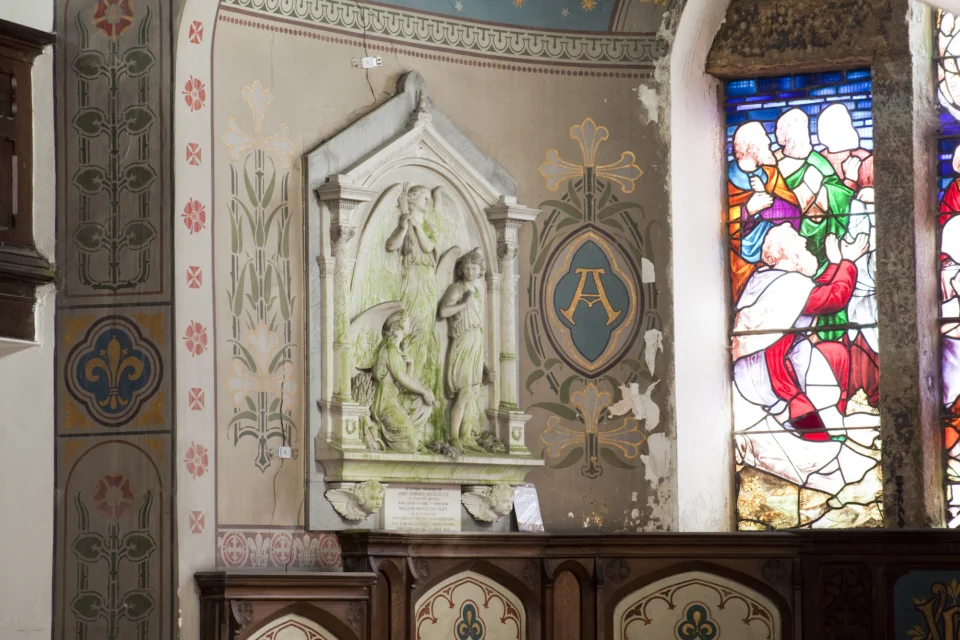 Ornate Wall Monument with angel. Wall Paintings blue with gold florals and red flowers. Edge of stained glass window visible depicting disciples.