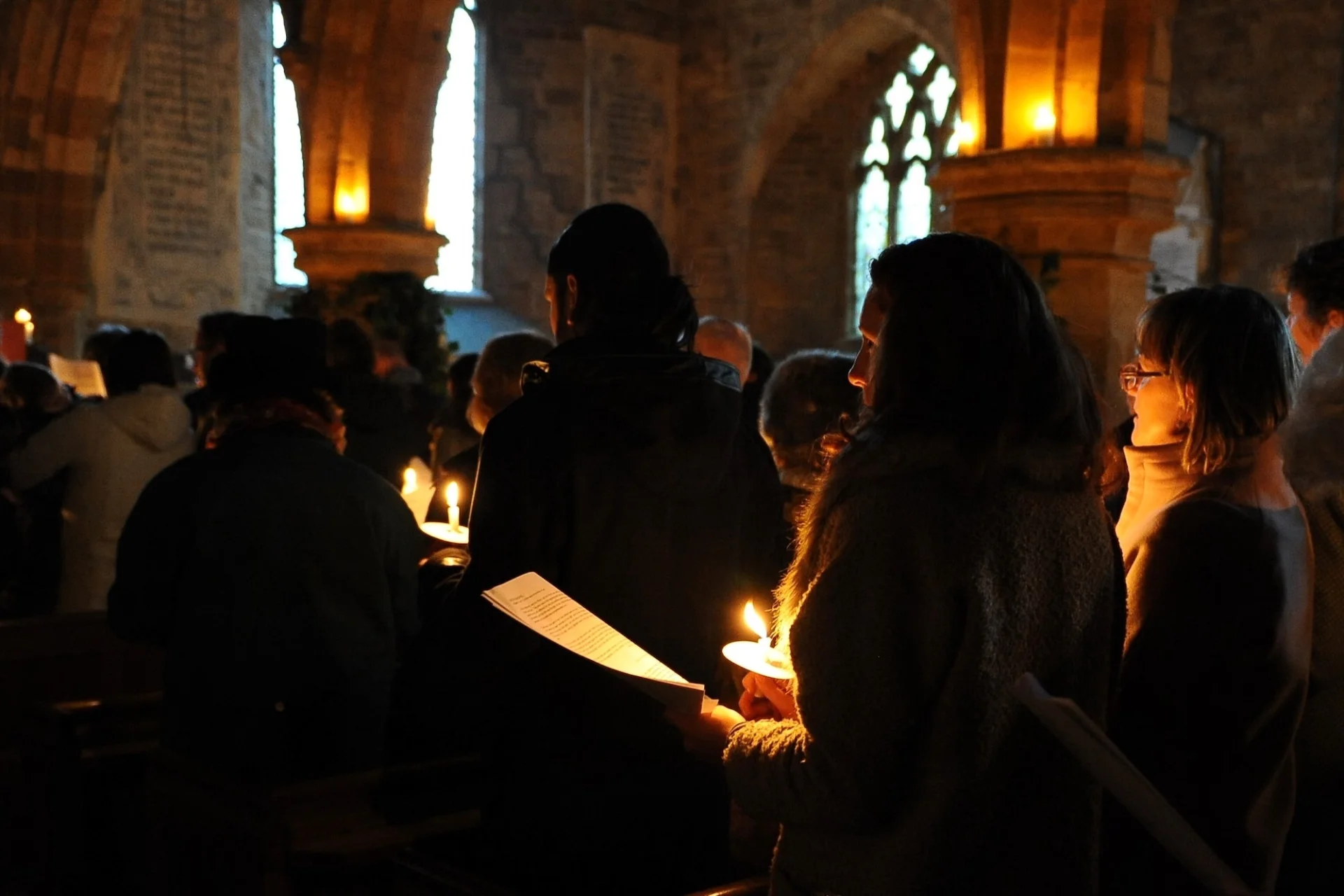 People singing in the candlelight church holding hymn sheets