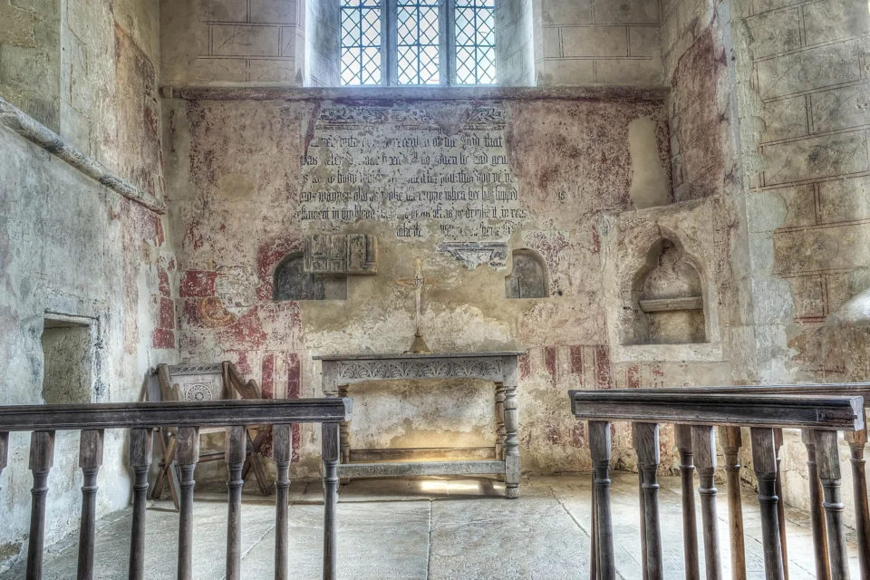layers of paintings including words and geometric designs over one another behind a simple wooden table, wooden gate and medieval style chair
