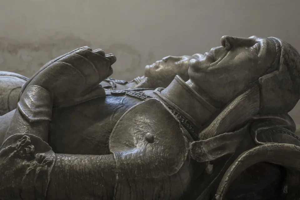 Stone carving monument of Sir John Curzon in full armour with his wife and their two dogs.