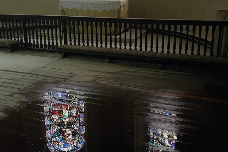 water on the wooden floor around the altar reflects two stained glass windows.