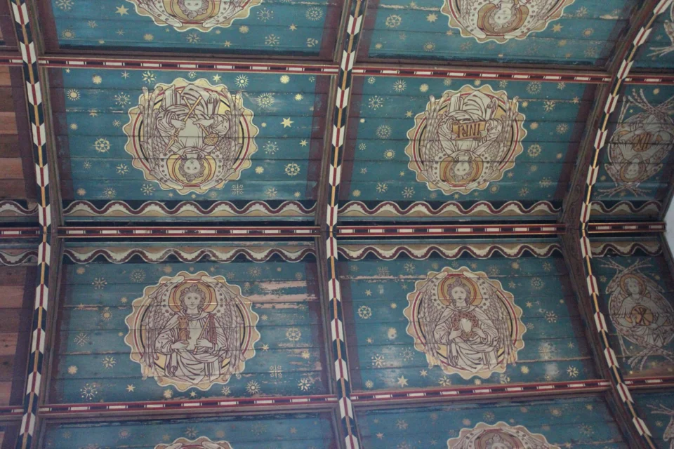 A wooden church ceiling painted to resemble a starry sky. Each panel contains the image of a golden saint on a circular medallion