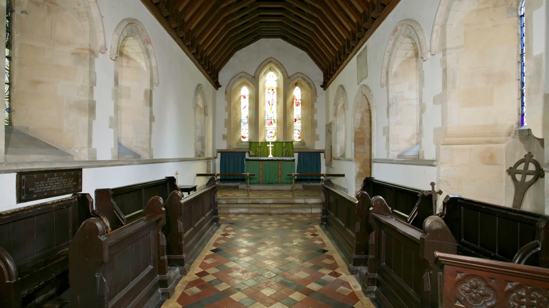 white washed walls, stained glass behind the altar, red and black tiles.
