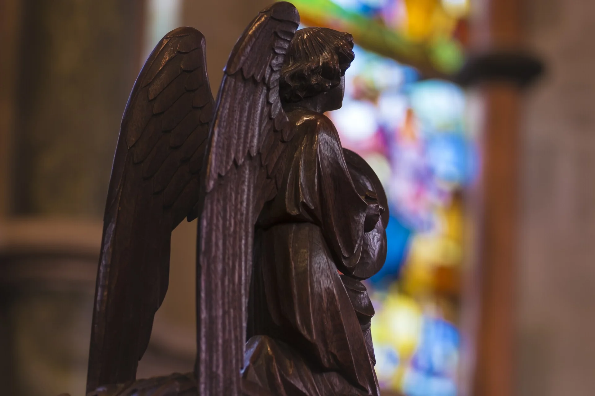 Wood carving depicting an angel with the stained glass window as background