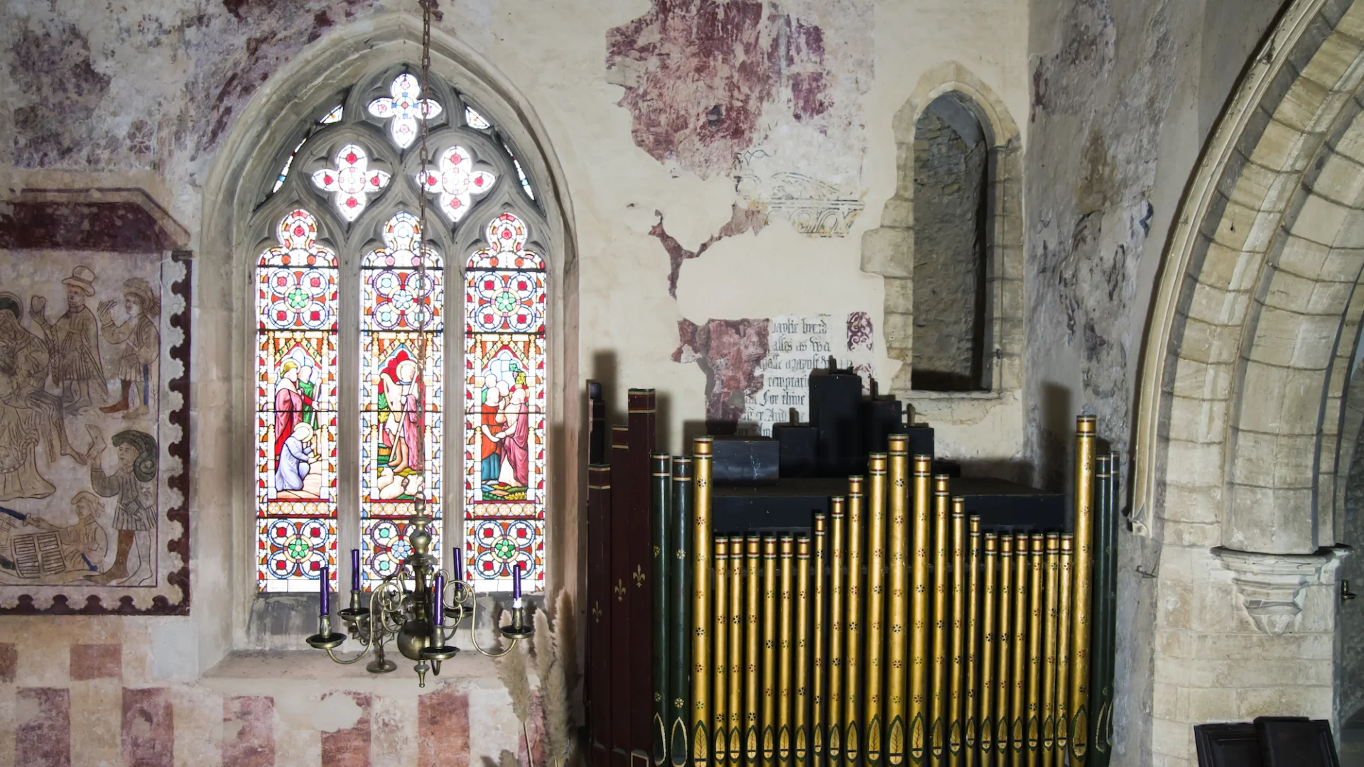 shows organ, highly colourful stained glass window and medieval wall paintings of people in reds and whites
