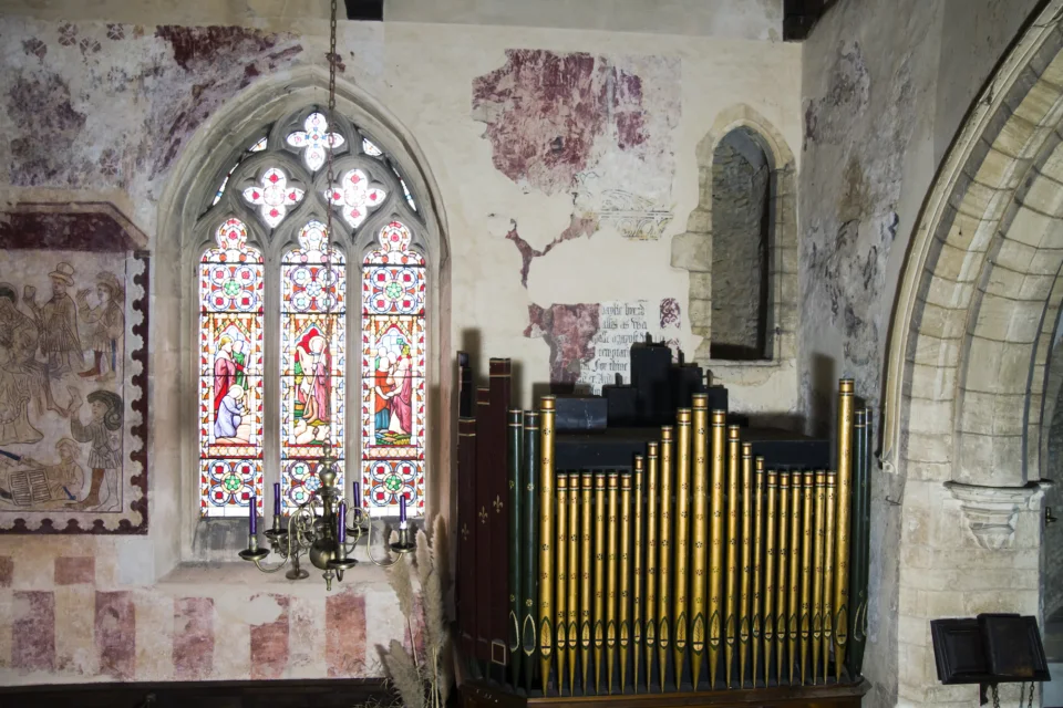 shows organ, highly colourful stained glass window and medieval wall paintings of people in reds and whites