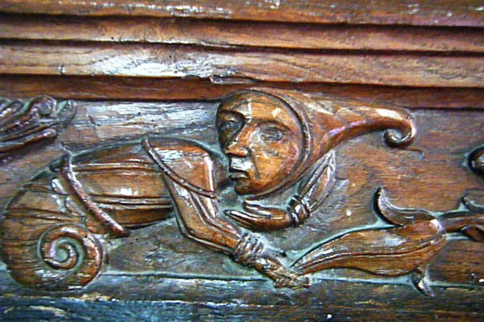 Medieval male figure with hat carved on back of wooden pew
