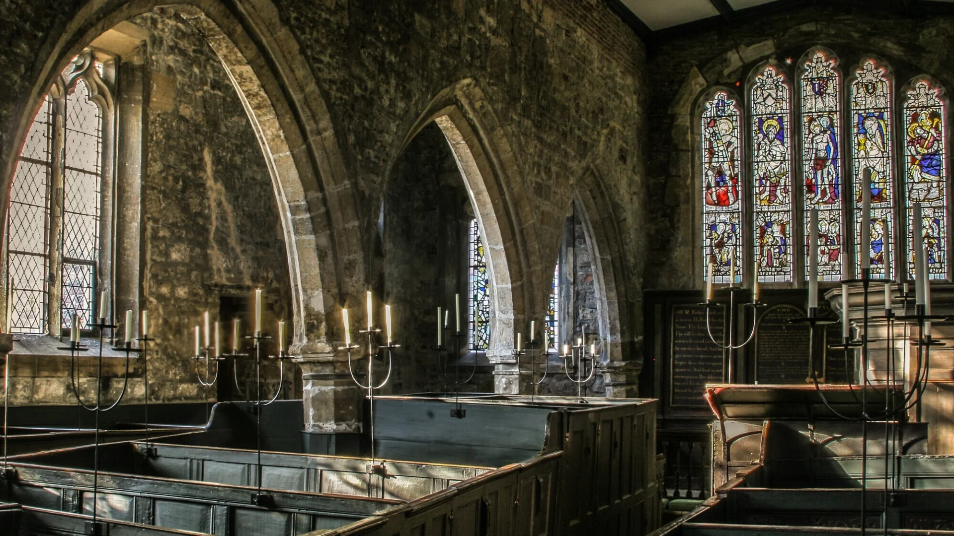 Atmospheric view of the interior with low light, carved stone arches, box pews and candle holders