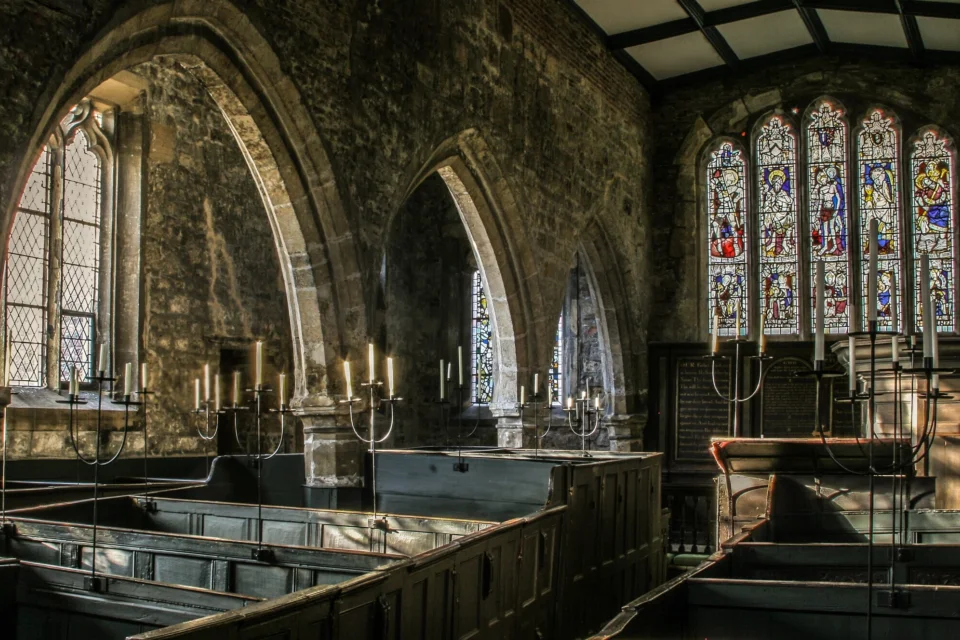 Atmospheric view of the interior with low light, carved stone arches, box pews and candle holders