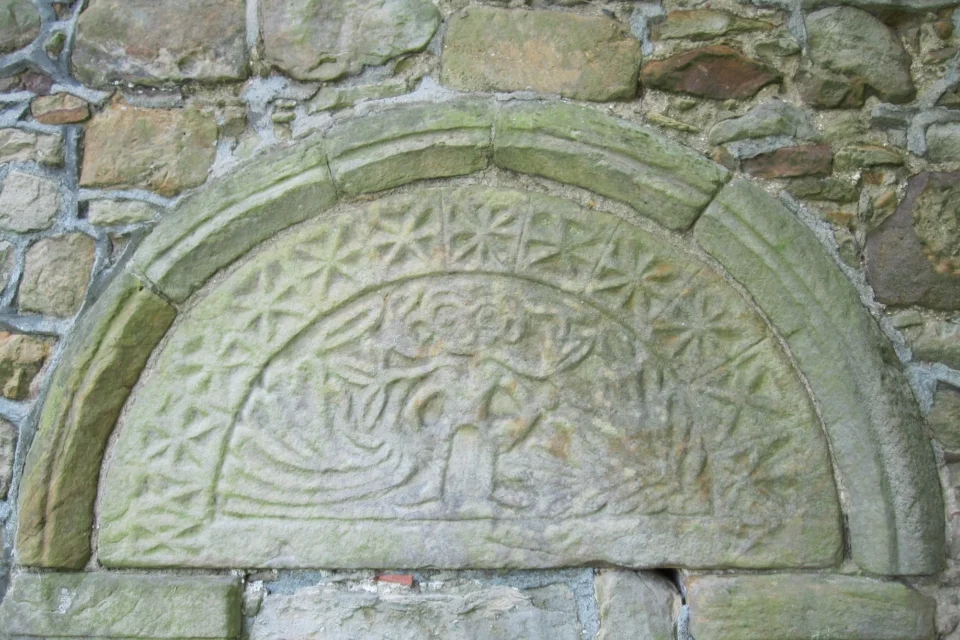 old stone typmpanum carved with vines, stars and the shape of a cartoonish man