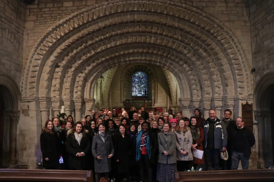 A group photo, around 25 staff are gathered under a stunning archway.