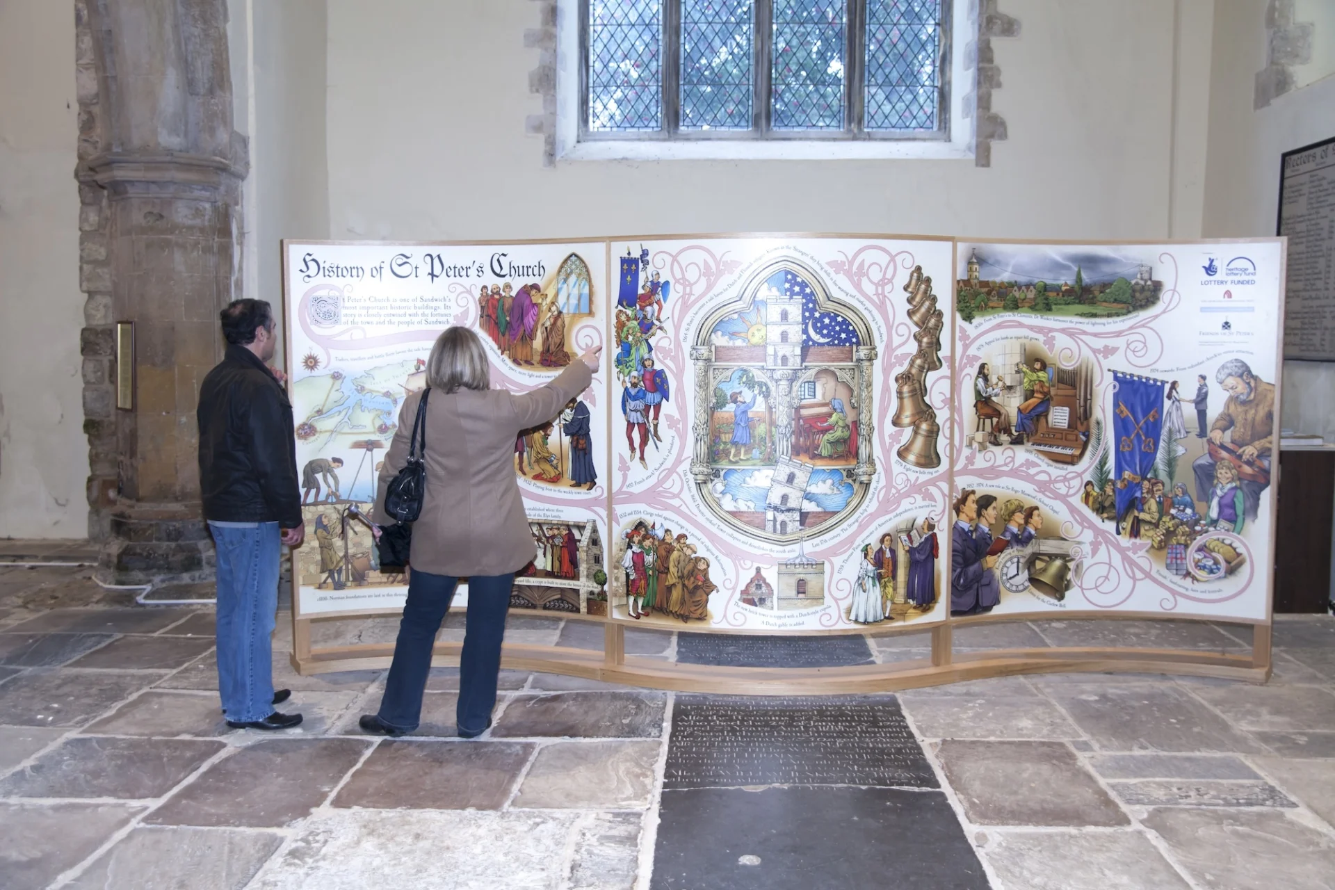 two visitors look at a large board covered in text and images depicting the history of the church