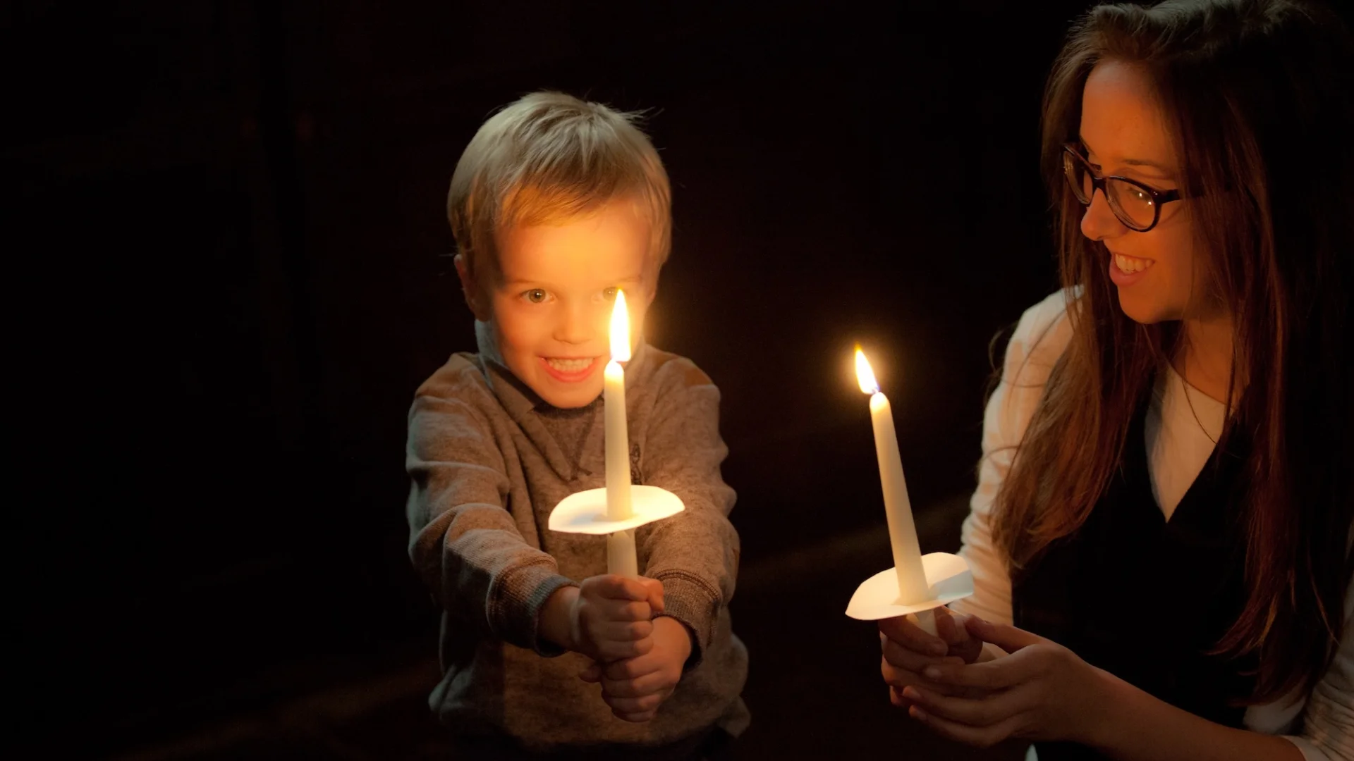 mum and son hold up candles in the dark