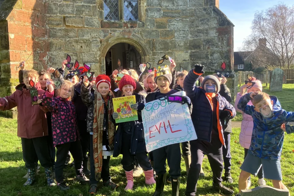 children dance in front of church in masks and with a sign saying 'Good triumphs over evil'