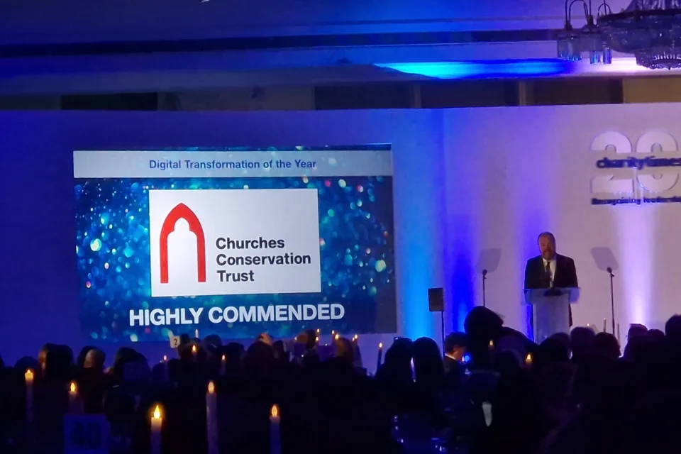 presentation with large screen with CCT logo a speaker and a large crowd watching and candles on the tables.