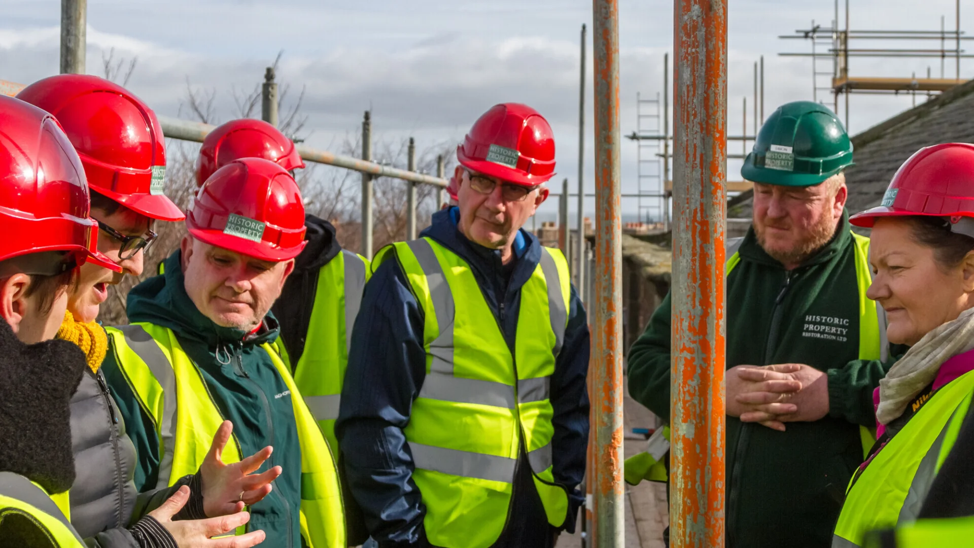 visitors in hard hats and high visibility tops listening to the tour guide and standing on the scaffolding