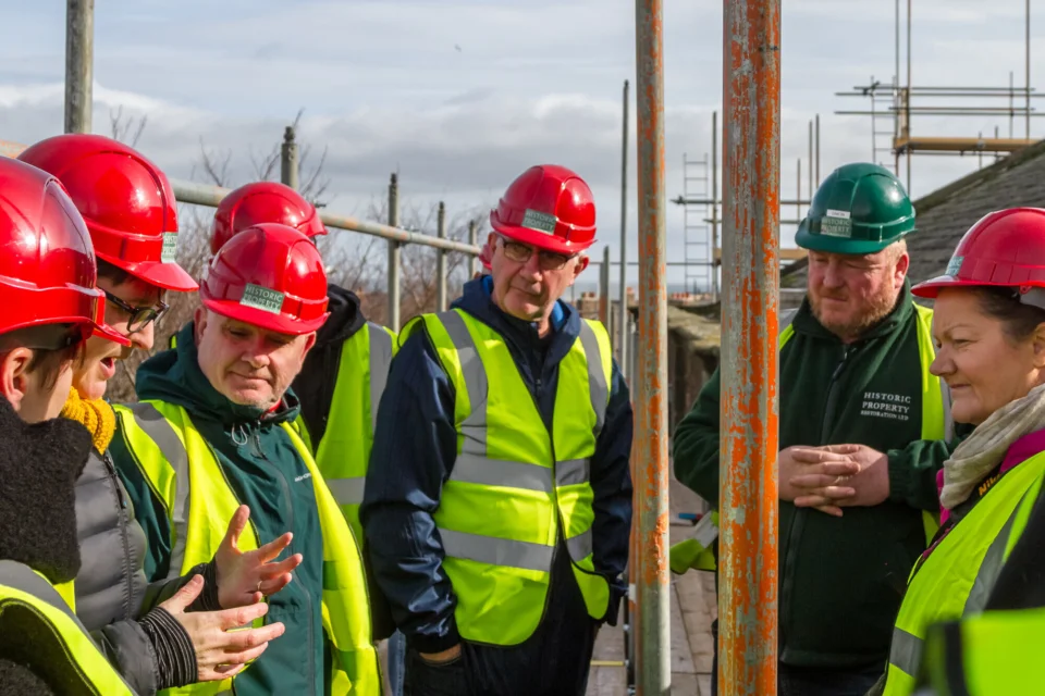 visitors in hard hats and high visibility tops listening to the tour guide and standing on the scaffolding