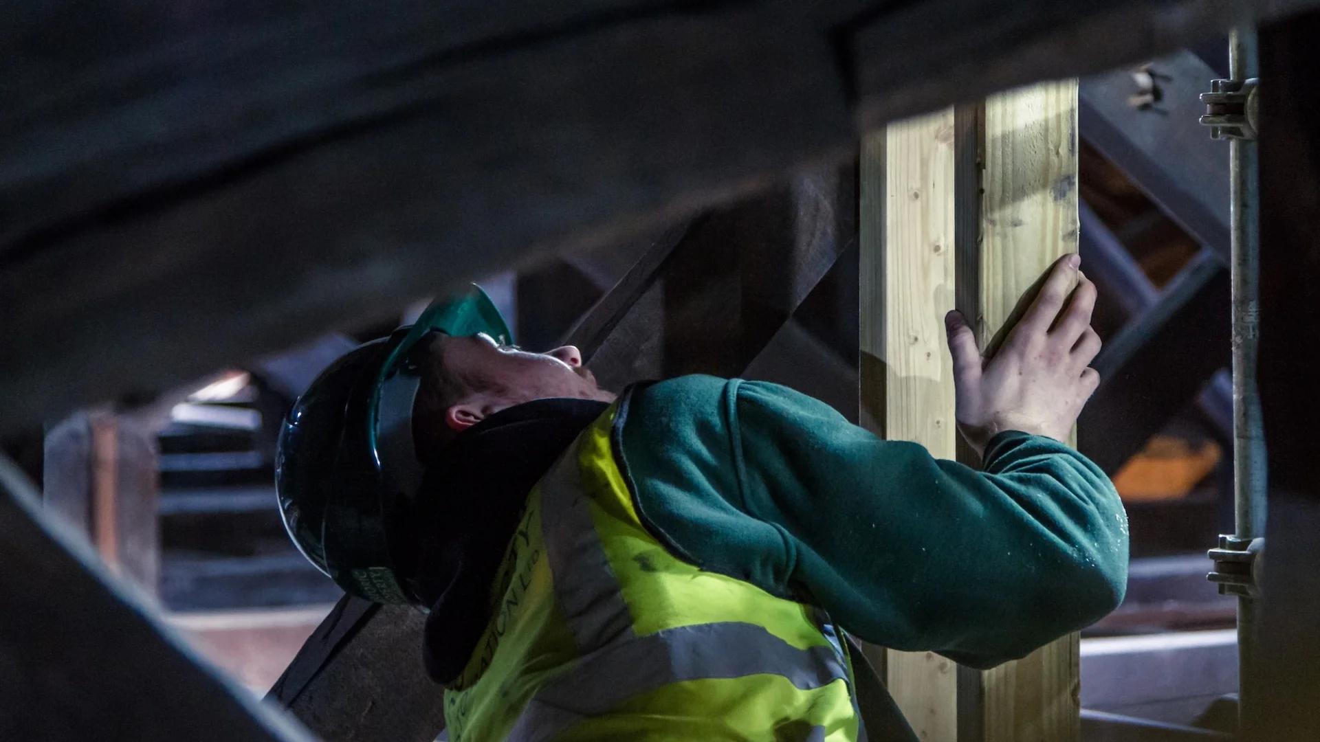 young worker in hardhat and high visibility jacket within the beams of a new roof