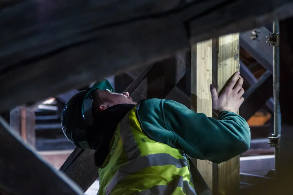young worker in hardhat and high visibility jacket within the beams of a new roof