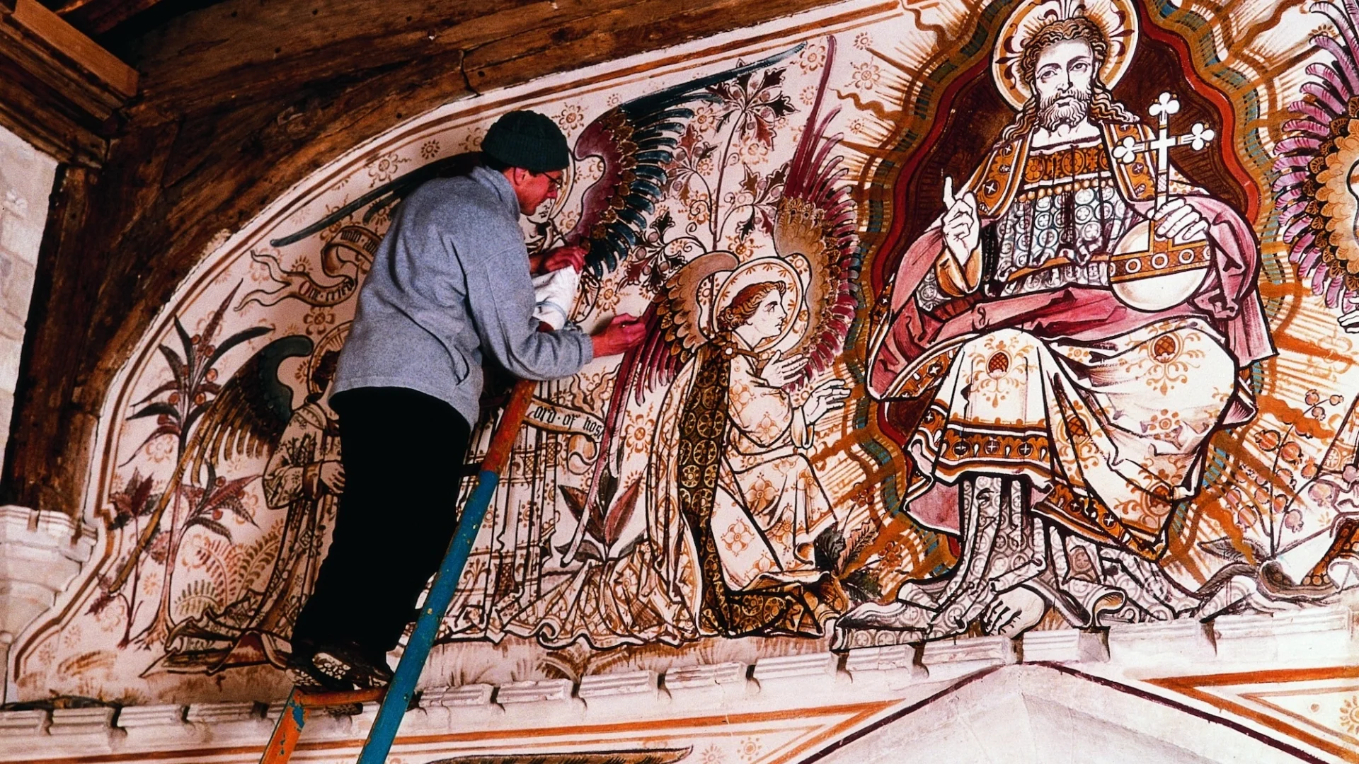 man on ladder is restoring vibrant red and gold wall paintings with Jesus (as King of heaven) at centre and an angel kneeling to him.