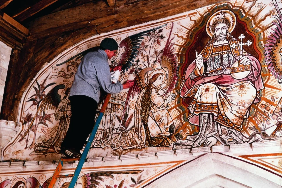 man on ladder is restoring vibrant red and gold wall paintings with Jesus (as King of heaven) at centre and an angel kneeling to him.
