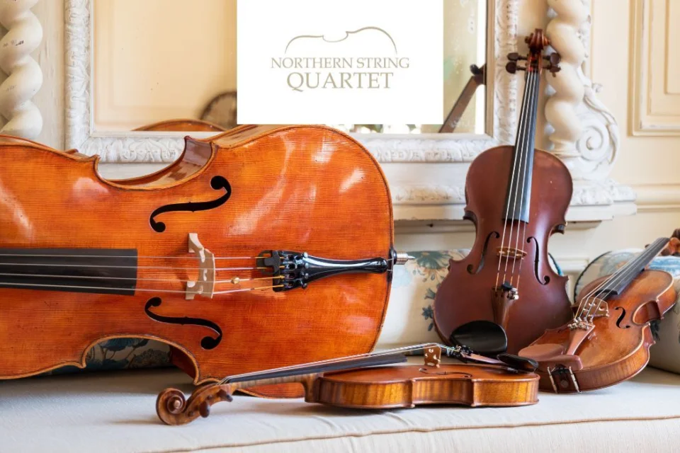 violins and cellos leant on the mantle in front of a mirror with the logo for the Northern String Quartet