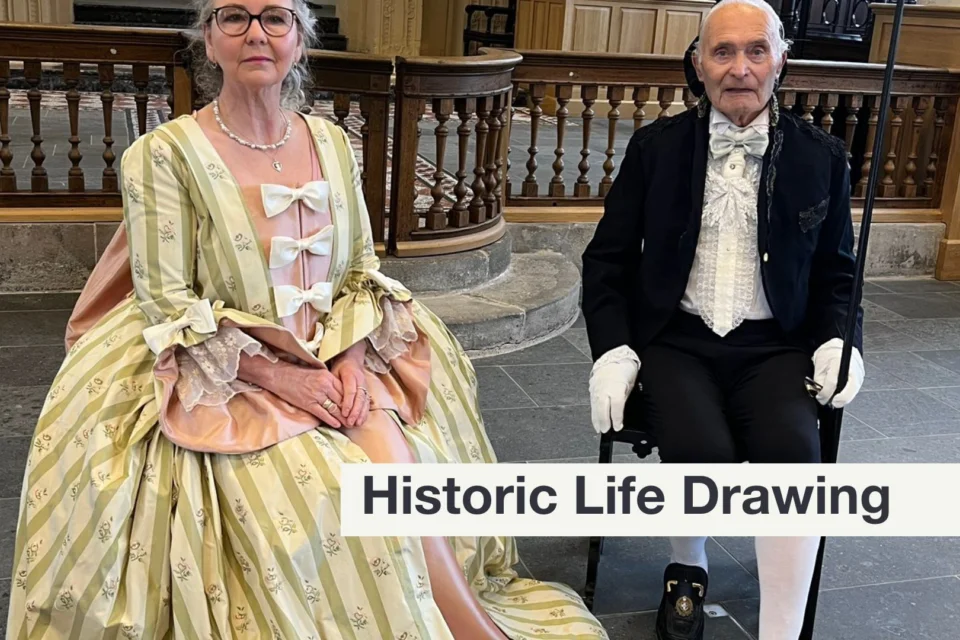 two sitters for the life drawing dressed in historical clothing. On the left a woman in a white and green striped dress. The man in a black suit with short trousers and long socks.