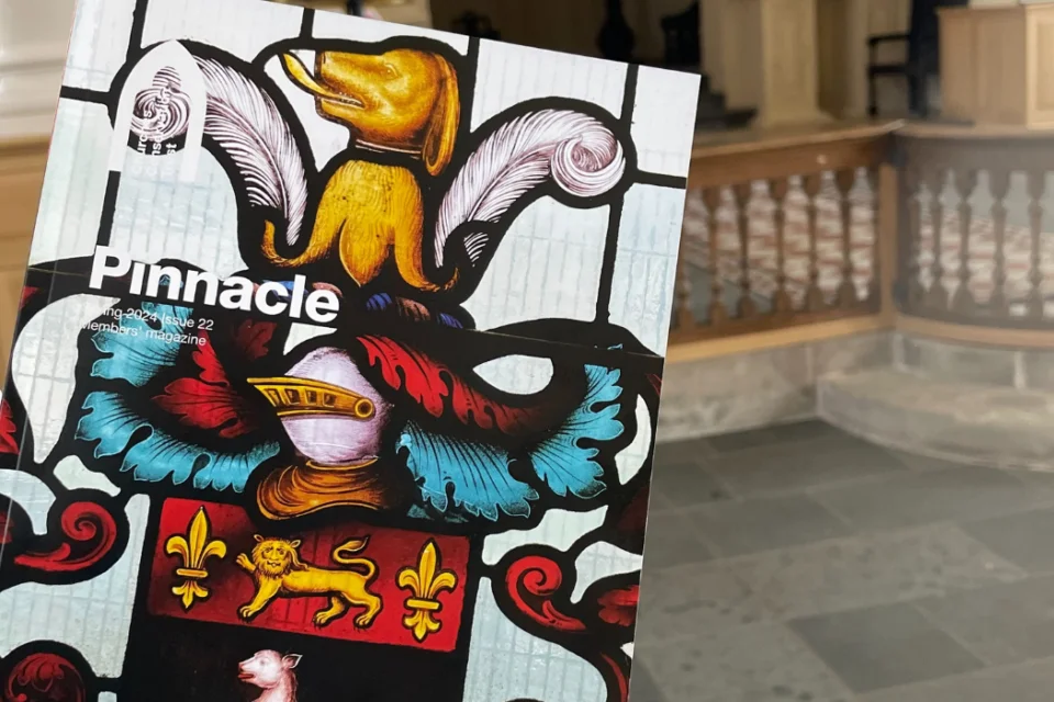photo of magazine held up in church, magazine cover image with heraldic image with helmet and large feathers above.