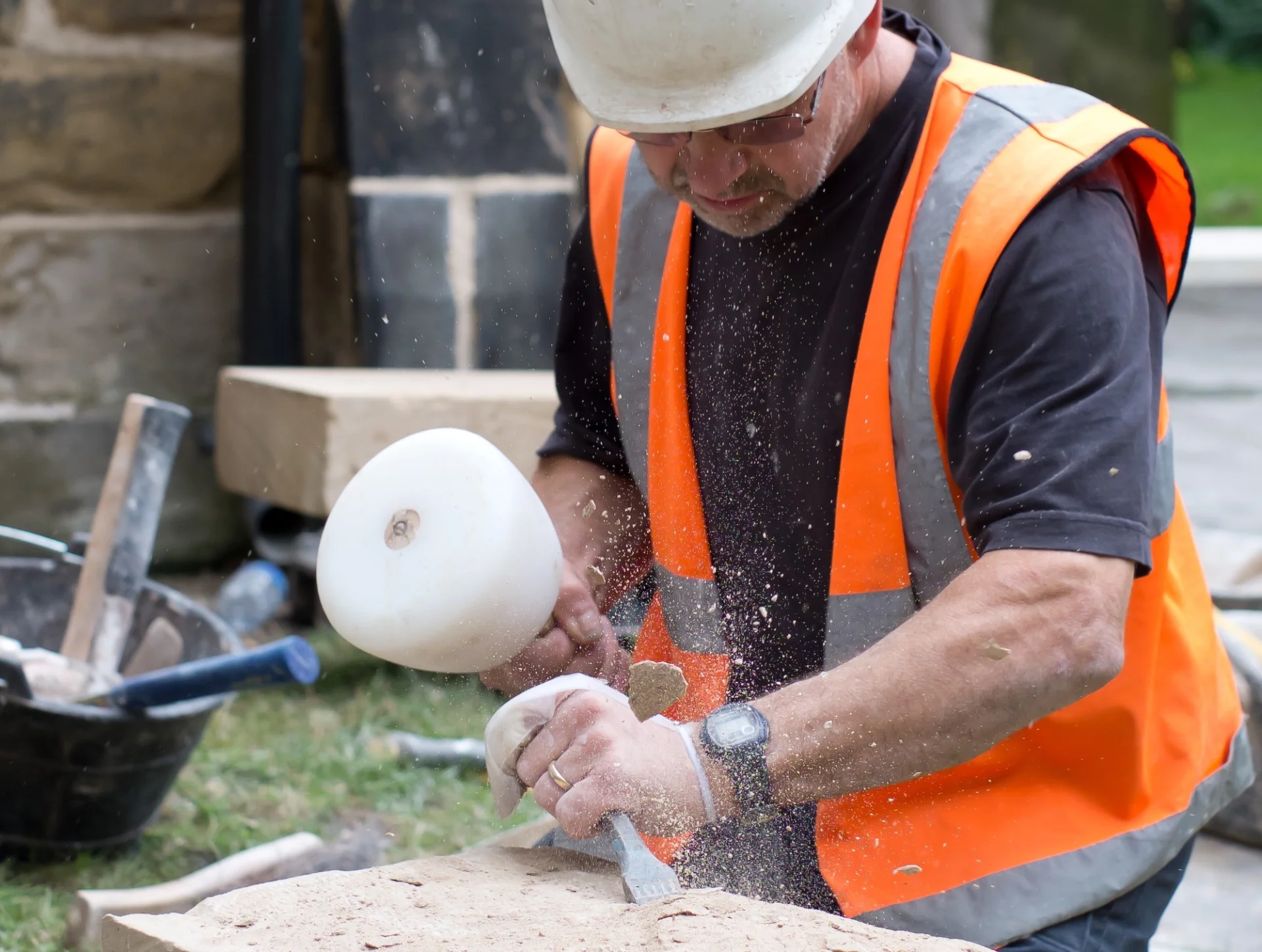 builder in hard hat and high visibility jacket chisels into stone