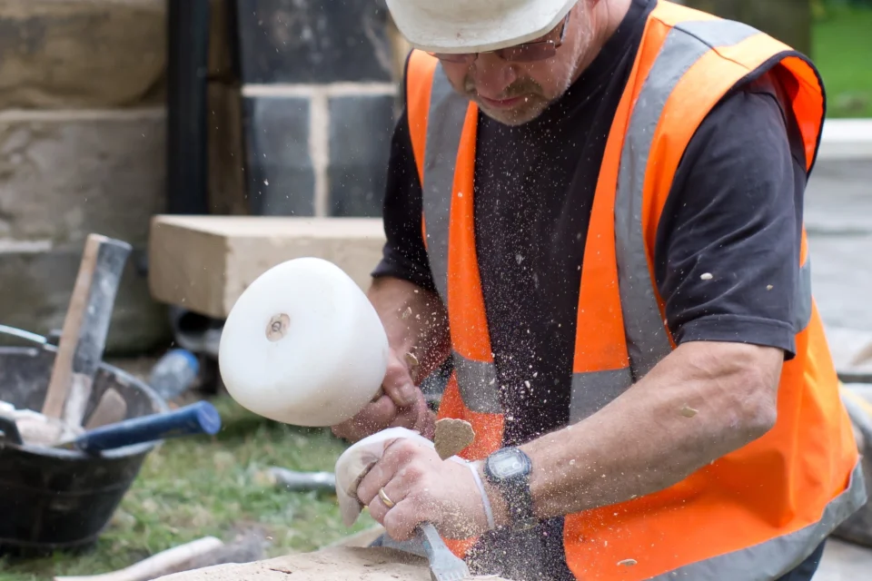 builder in hard hat and high visibility jacket chisels into stone